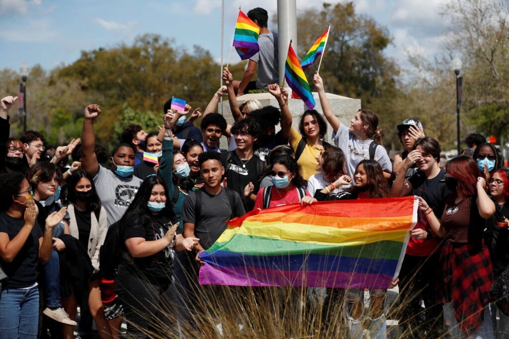 high school students with rainbow flag in front and waving rainbow flags in the back